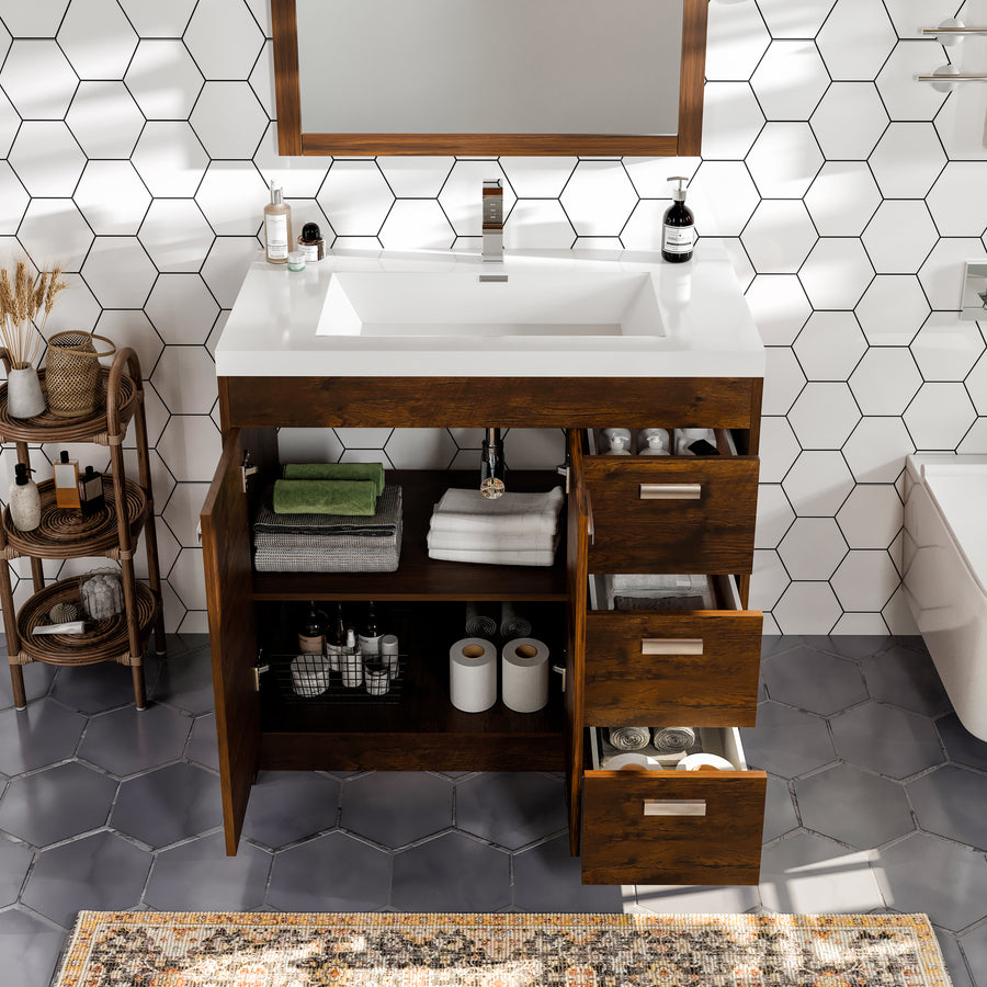 A modern bathroom vanity with a white sink, open wooden drawers and cabinet revealing neatly folded towels, toiletries, and toilet paper, set against a hexagonal white tile wall.