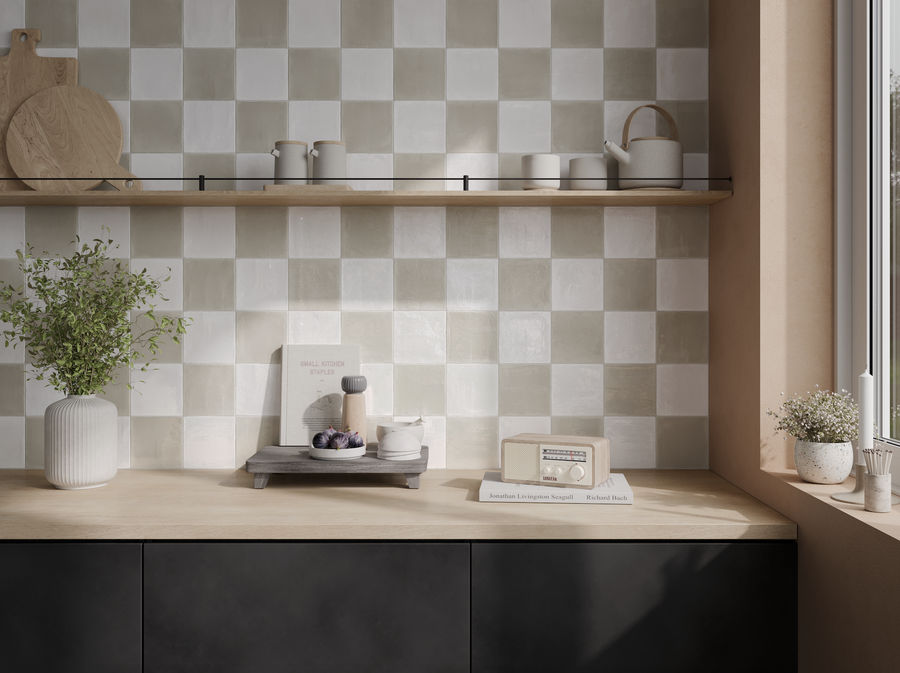 A modern kitchen features a light wood countertop, Harmony 5x5 Porcelain Tile backsplash in a checkerboard pattern, potted plants, kettle, cups, books, and a window streaming in natural light.