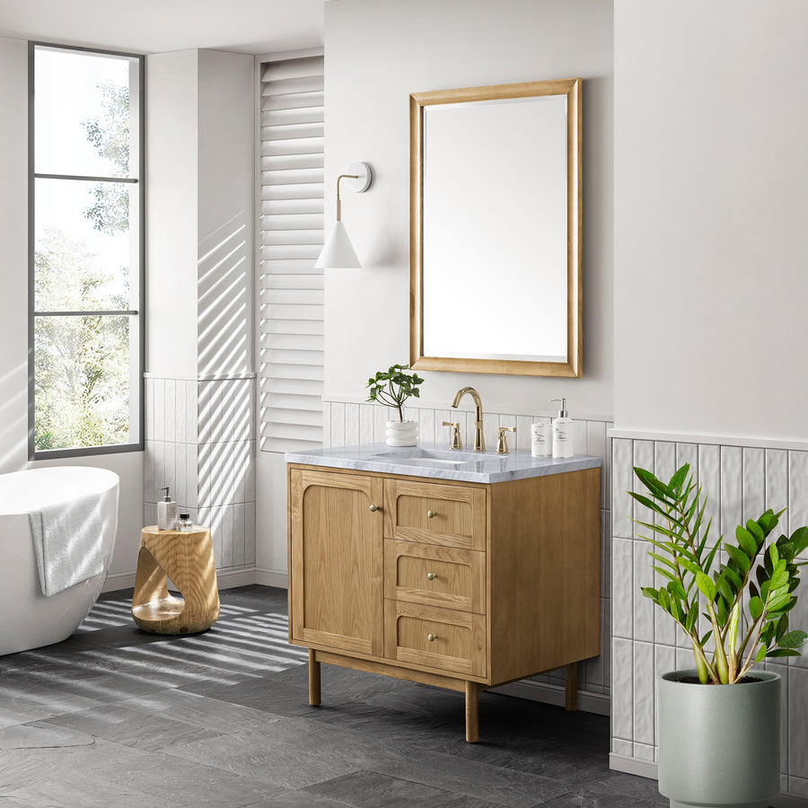 A modern bathroom with a freestanding tub, wooden vanity with marble countertop, large mirror, potted plant, small wooden stool, wall sconce, and large window letting in natural light.