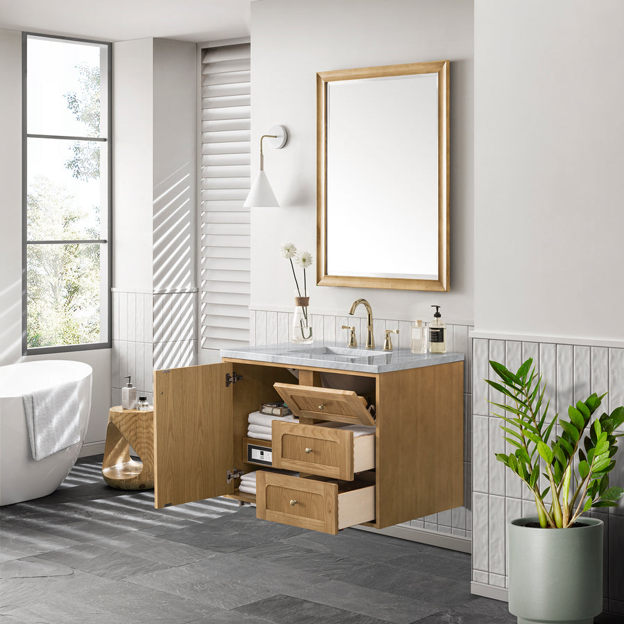 A modern bathroom with a floating wooden vanity cabinet, drawers open to show organized storage, a round bathtub, a large mirror, a potted plant, and natural light from a window.