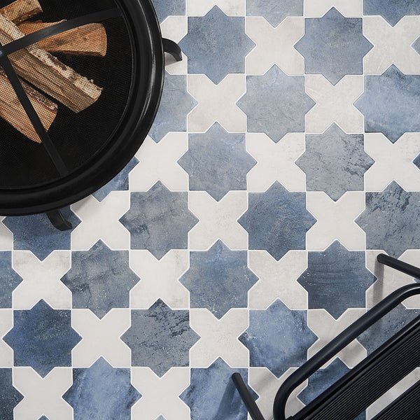 Blue and white geometric patterned tile floor with a black metal fire pit containing firewood in the top left corner and part of a black metal chair in the bottom right corner.