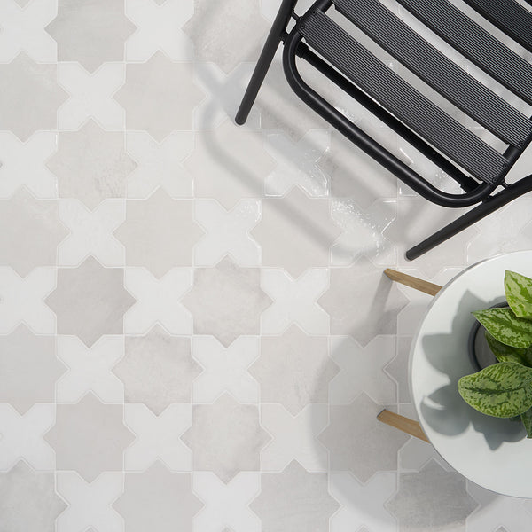 A black metal chair and a potted plant sit on a tiled floor with a geometric white and light gray pattern resembling interlocking crosses.