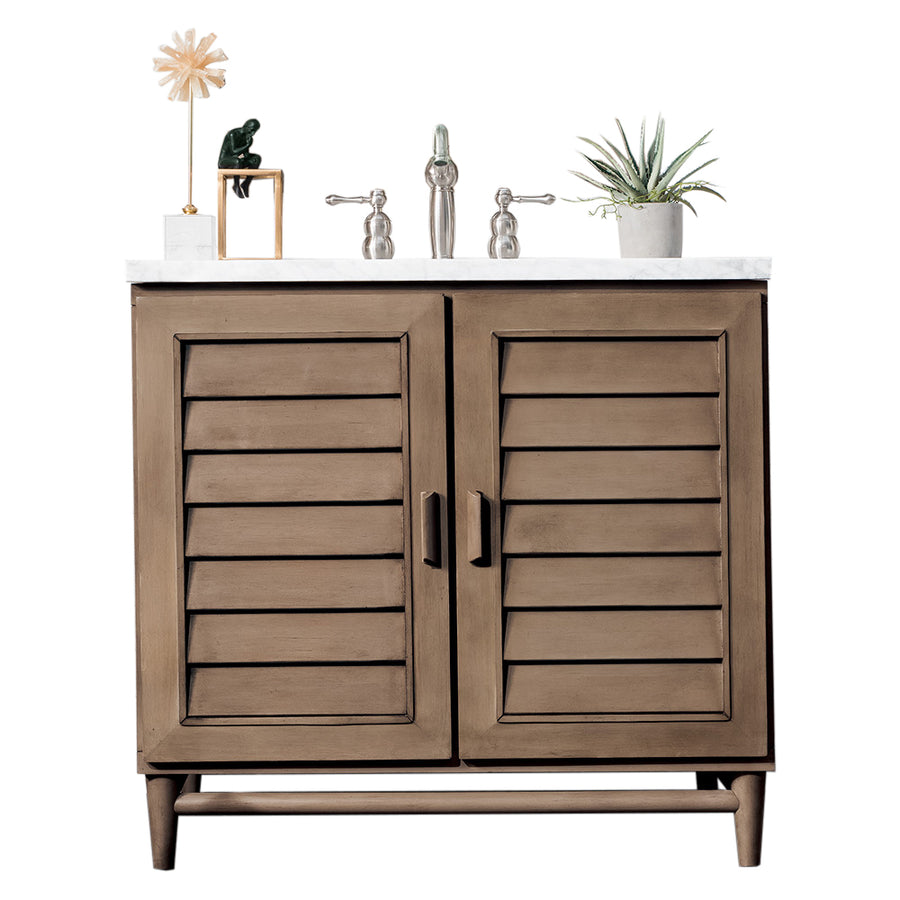 A wooden bathroom vanity with two louvered doors, a white countertop, silver faucet, and handles. Decor items on top include a small plant, a green ornament, and a decorative starburst sculpture.