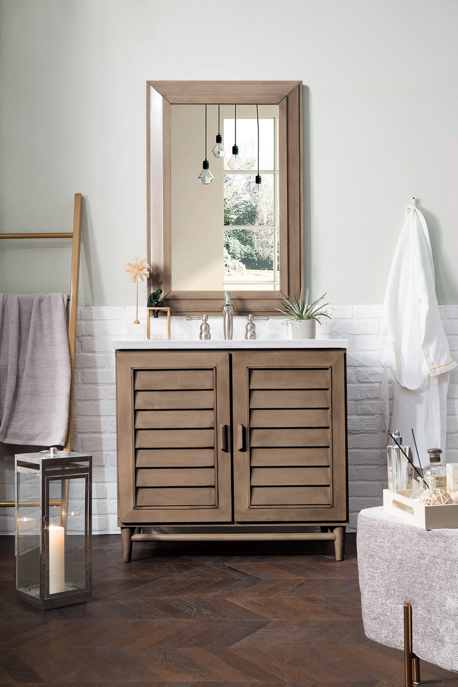 A modern bathroom showcases the Portland 36" Vanity with louvered doors, topped by a large framed mirror, paired with a silver faucet, pendant lights, decorative plants, towels on a rack, a candle lantern, and ample floor basket storage.
