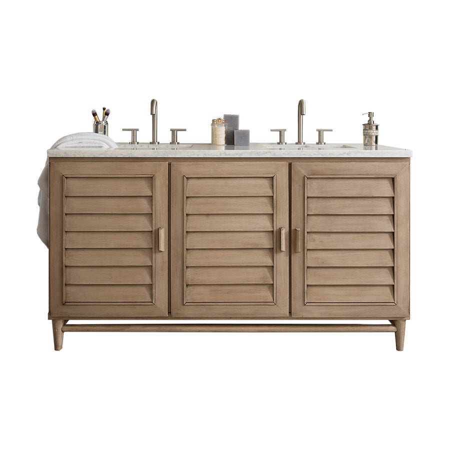 A wooden bathroom vanity with three shutter-style cabinet doors, a white countertop, dual faucets, and various bathroom accessories on top, including towels, toothbrush holder, and soap dispenser.