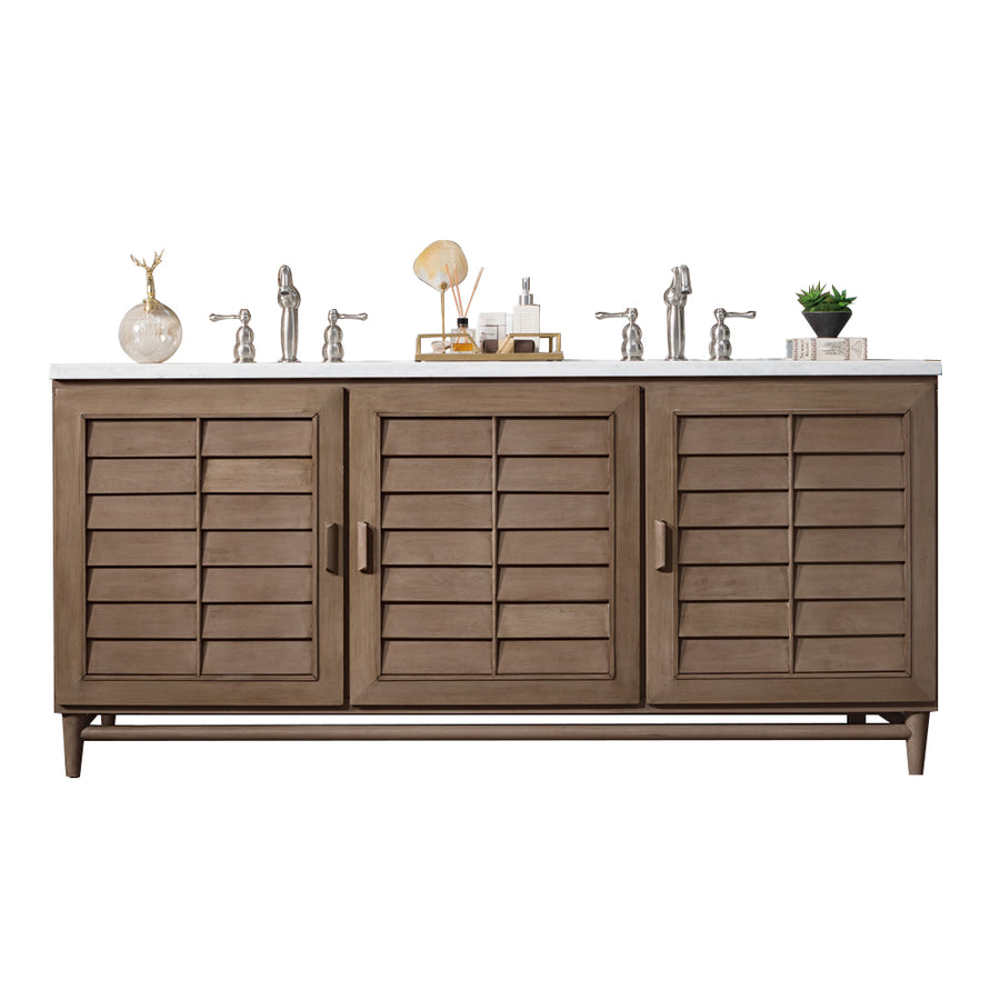 A wooden bathroom vanity with three shutter-style cabinet doors, a white countertop, two sinks with silver faucets, and decorative items including a plant, soap dispensers, and a small deer figurine.