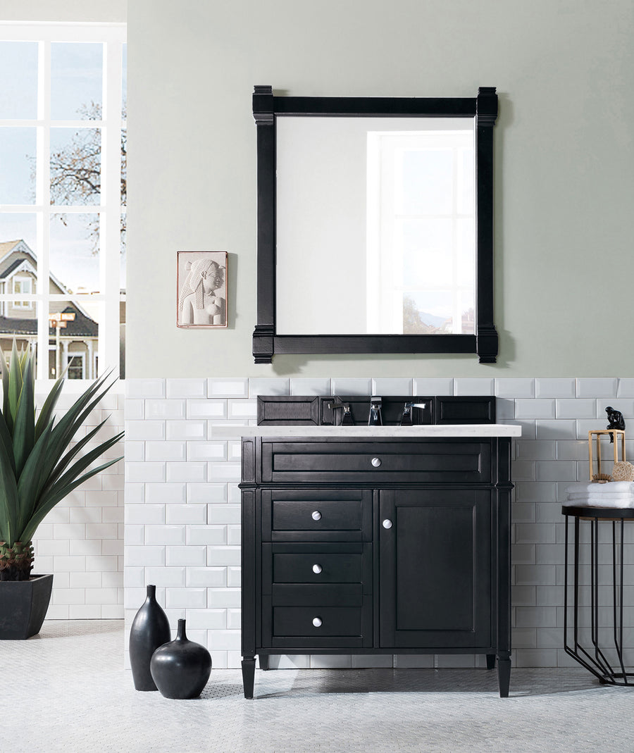 A modern bathroom showcases the Brittany 36" Vanity with a white countertop, a large square mirror, subway tile walls, decorative vases, a plant, a stool, and natural light streaming through the window.