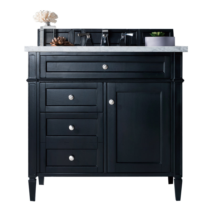 A black bathroom vanity with a white marble top, silver knobs, three drawers, one cabinet door, a rectangular sink, and decorative items including a plant and coral on the countertop.