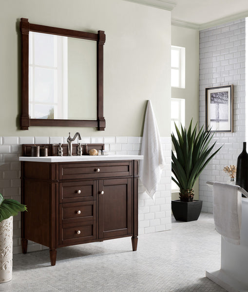 A modern bathroom with a dark wood vanity, white countertop, rectangular mirror, towel hanging on the wall, potted plant, and white subway tile accents. Natural light streams in from large windows.