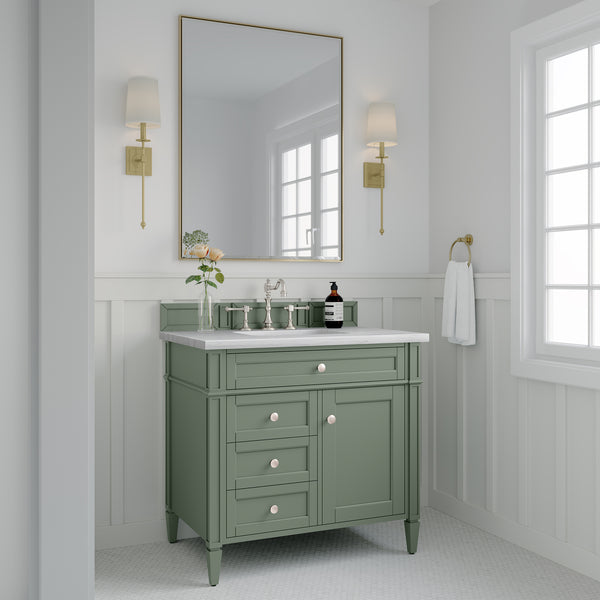 A bathroom with a sage green vanity, white countertop, and silver faucet sits below a large rectangular mirror. Two wall sconces flank the mirror. White walls, wainscoting, and a towel hang by a window.