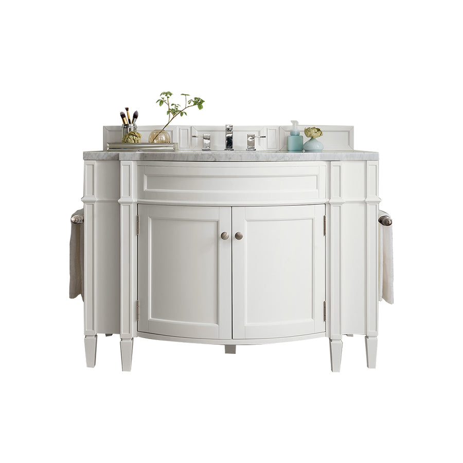 The Brittany 46" Vanity is a white hardwood bathroom cabinet with a marble countertop, two cabinets, silver handles, and side towel bars. The counter holds a plant, toiletries, and a glass tray with brushes against a white backdrop.