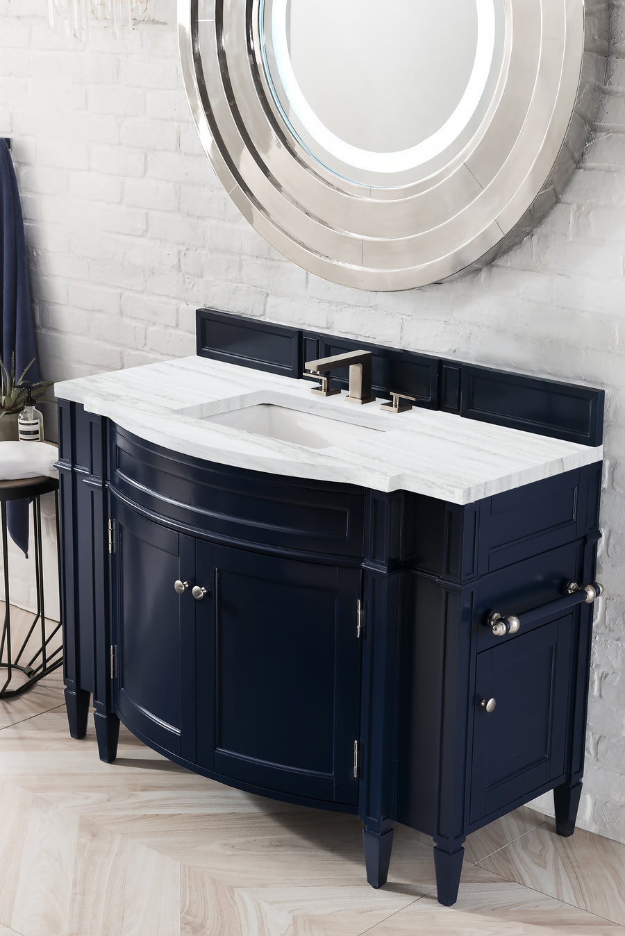 A modern bathroom vanity with a glossy navy blue cabinet, white marble countertop, rectangular sink, and silver faucet, set against a white brick wall with a large round mirror above.
