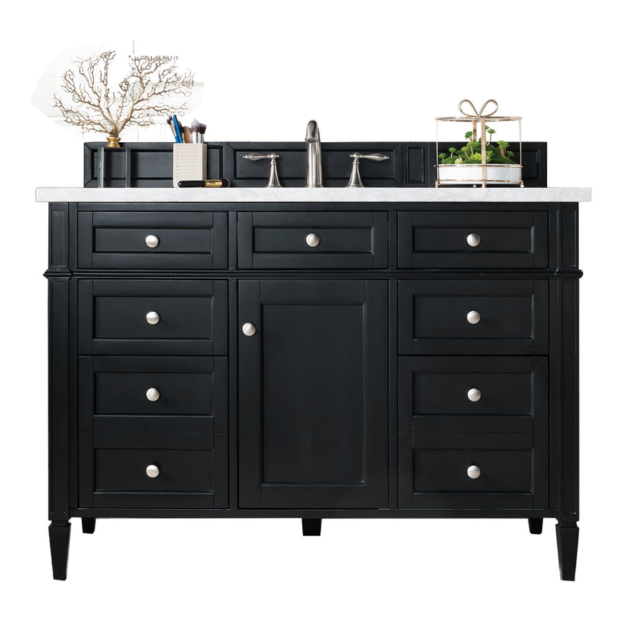 A black bathroom vanity with silver knobs, a white countertop, a modern faucet, and small decorative items, including a plant and coral, arranged on top. Multiple drawers and a central cabinet offer storage space.