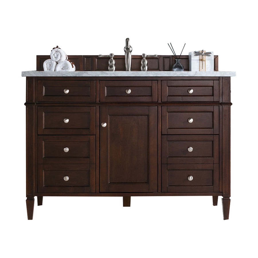 A dark wood bathroom vanity with silver knobs, a white marble countertop, a modern faucet, and decorative items including a towel, diffuser, and wrapped gift on top.