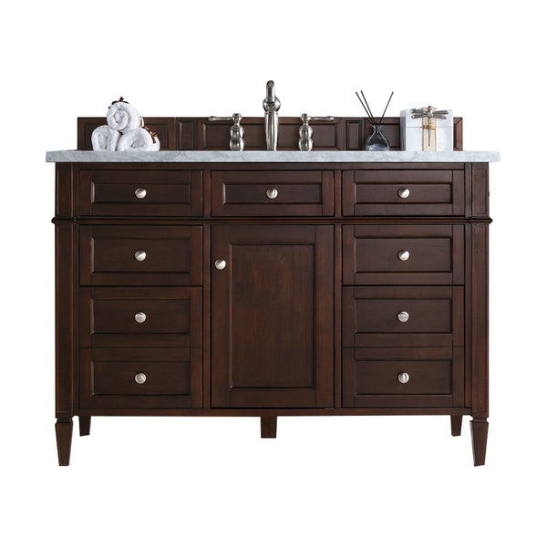 A dark wood bathroom vanity with silver knobs, a white marble countertop, a modern faucet, and decorative items including a towel, diffuser, and wrapped gift on top.