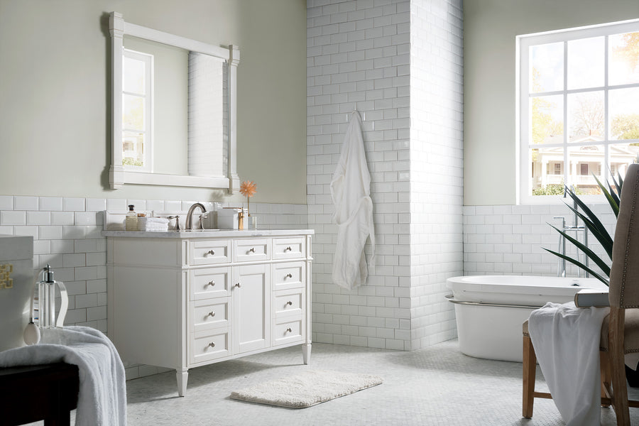 Bright, modern bathroom with a large window, white vanity and sink, wall mirror, white tiles, a towel hanging on the wall, a toilet, a small rug, and a potted plant in the corner.