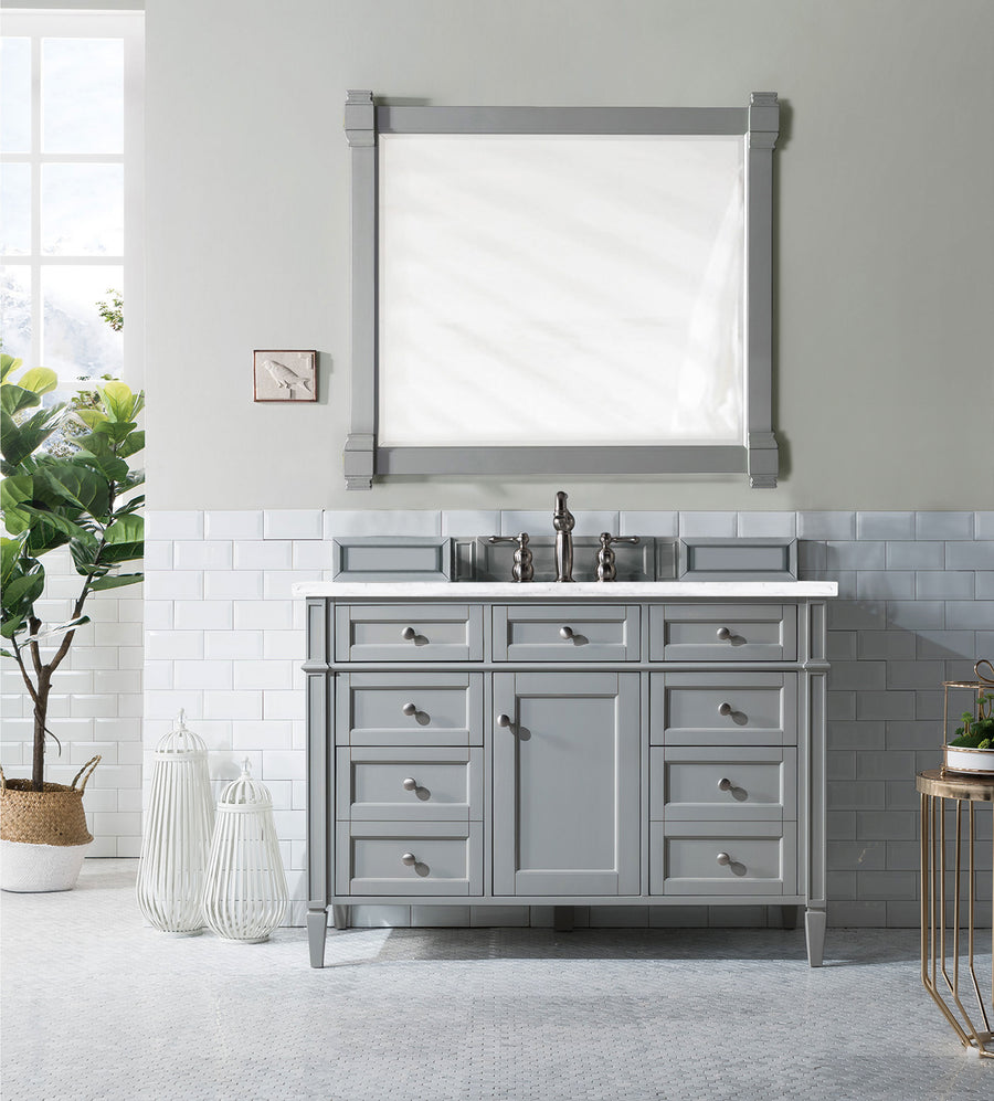 A modern bathroom features the Brittany 48" Vanity with a white countertop, a large framed mirror, white tile and light gray walls, plus a plant, birdcages, and a small clock for a complete luxury look.