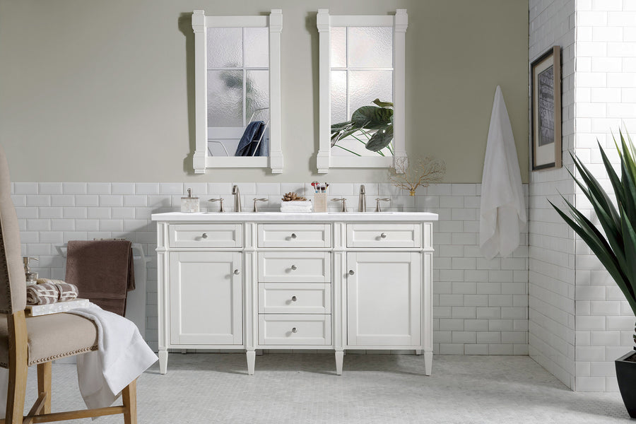 A bright, modern bathroom features a Brittany 60" Double Bowl Vanity with dual sinks, white cabinetry, two mirrors, subway tile walls, a towel on a hook, a potted plant, and a cushioned chair with folded towels.