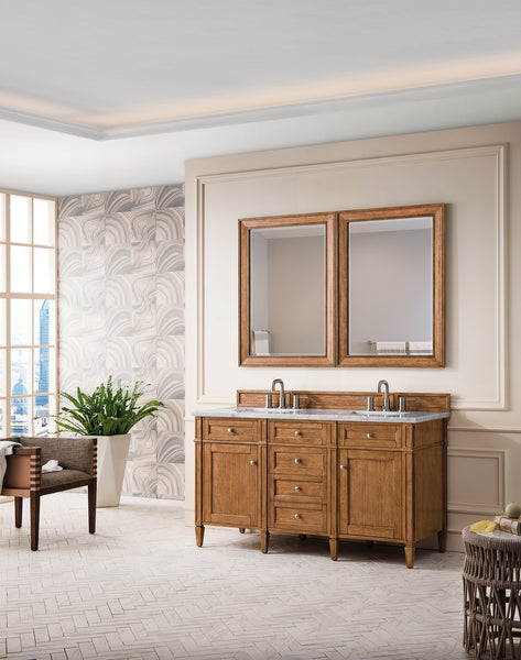 A modern bathroom features a double wooden vanity with two sinks and matching mirrors, neutral walls with patterned wallpaper, a potted plant, a wicker chair, and a laundry basket in the corner.