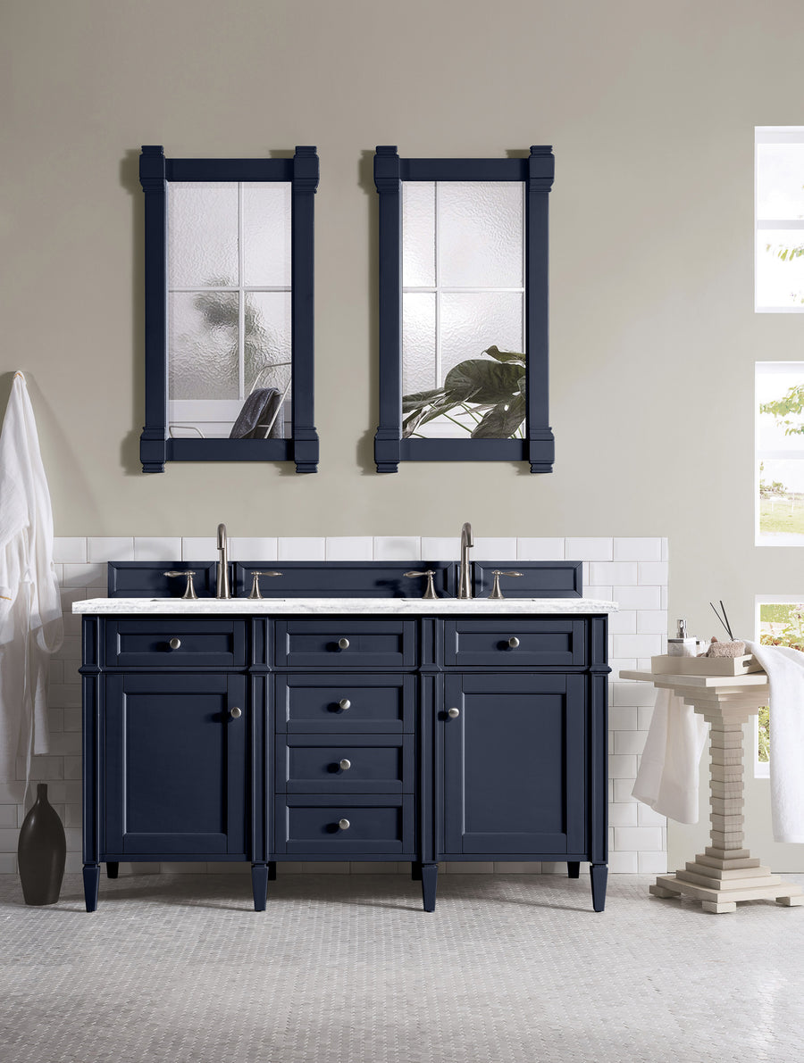 A modern bathroom showcases the Brittany 60" Double Bowl Vanity in navy blue, paired with double sinks, two framed mirrors, a white tile backsplash, light gray walls, natural light from small windows, a left-side towel, and a plant on the right table.