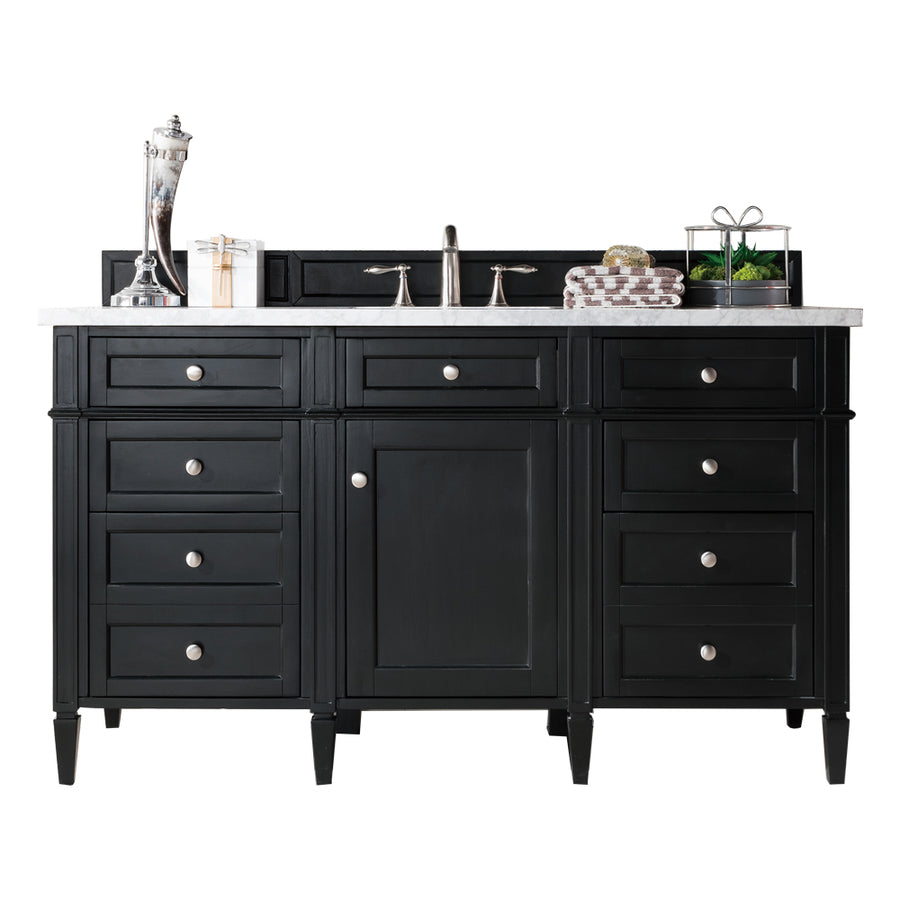 A black bathroom vanity with a white countertop, silver faucet, and cabinet hardware. Decorative items, including a silver vase, small box, gift, and plant, are arranged on the counter.