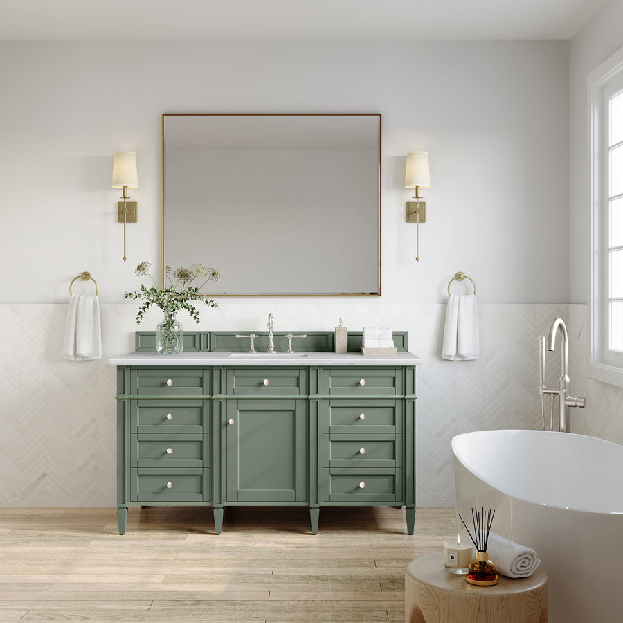 A modern bathroom showcases the Brittany 60" Vanity with a spacious green double-sink, a large mirror above, brass fixtures, wall sconces, a white freestanding tub, abundant natural light, and neatly arranged towels with decorative accents.