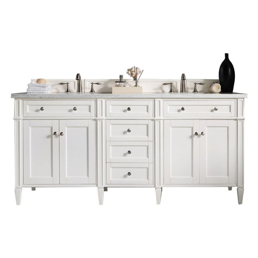 A double-sink white bathroom vanity with shaker-style cabinets, four central drawers, a marble countertop, two faucets, and decorative items including towels, seashells, and a black vase.