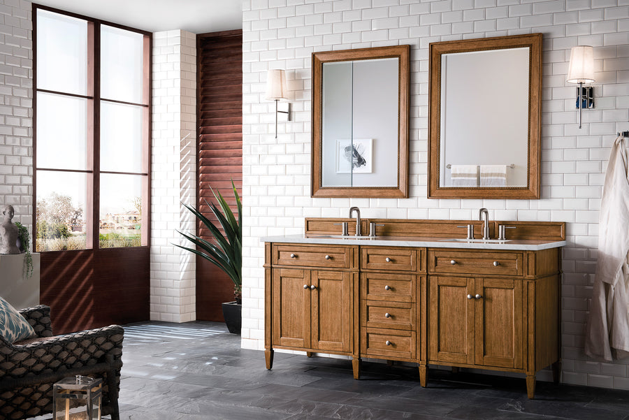 A modern bathroom with white subway tile walls, a double-sink wooden vanity, two mirrors, wall sconces, large windows, a potted plant, and gray tile flooring.