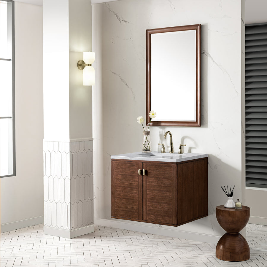 A modern bathroom features a wall-mounted wooden vanity with a marble countertop, a rectangular mirror with a matching wooden frame, a brass faucet, and light fixtures. A small round table holds decor items nearby.