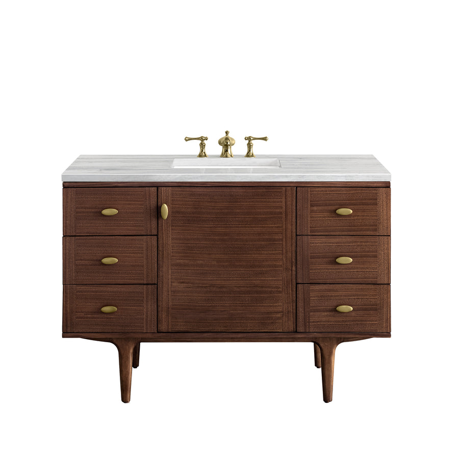 A mid-century modern wooden bathroom vanity with a white countertop, brass faucet, and six drawers with brass knobs, standing on four tapered legs.