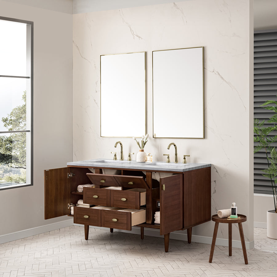 A modern bathroom vanity with a white countertop, dual sinks, gold fixtures, and open brown wood drawers and cabinets. Two rectangular mirrors hang above. A small plant and stool with toiletries are nearby.