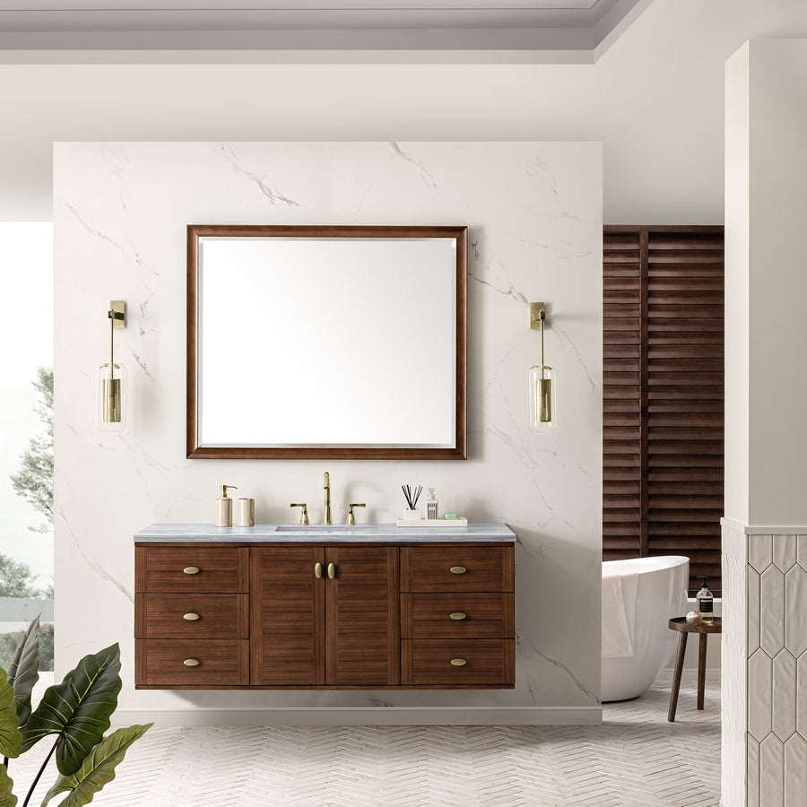 Modern bathroom with a wooden vanity, brass fixtures, large mirror, and pendant lights. White marble wall, herringbone tile floor, bathtub, wooden blinds, and a green plant are also visible.