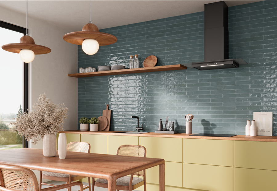 A modern kitchen features pale yellow cabinets, a wooden dining table with chairs, pendant lights, a blue tiled backsplash, open shelves with dishes, and a large window letting in natural light.