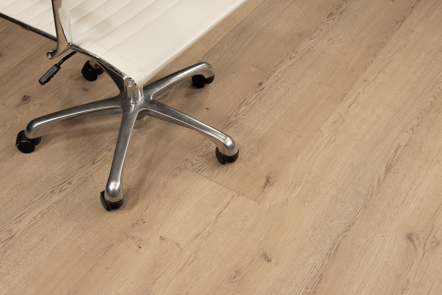 A partial view of a modern office chair with a white seat and metal base on black wheels, positioned on a light wood floor.