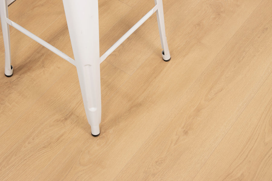 A close-up of light wood flooring with part of a white metal chair visible in the upper left corner of the image.