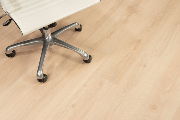 A close-up view of a light wood floor with part of a modern office chair featuring a chrome base and white cushioned seat.