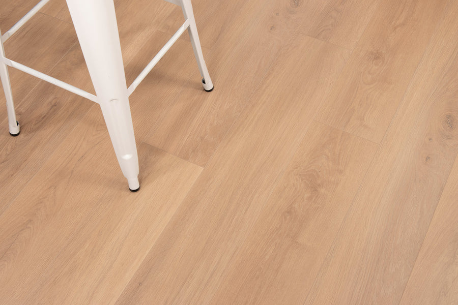A close-up of light wood flooring with a portion of a white metal chair leg visible in the upper left corner. The floor features a natural grain pattern and a smooth finish.