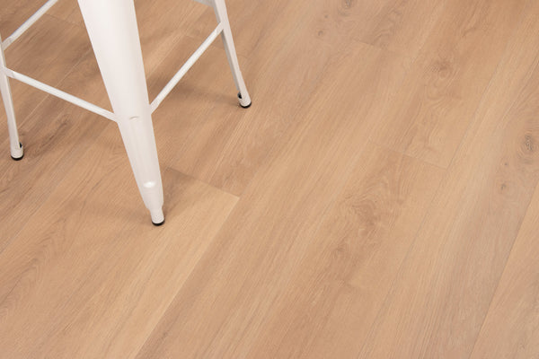 A close-up of light wood flooring with a portion of a white metal chair leg visible in the upper left corner. The floor features a natural grain pattern and a smooth finish.