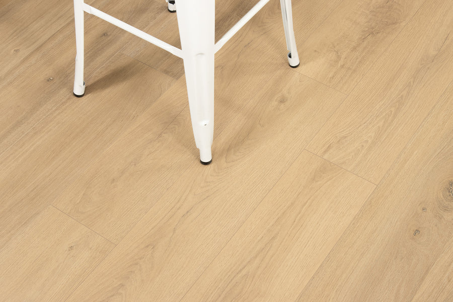 A white metal chair with thin legs sits on light wood grain flooring. The photo focuses on the flooring’s texture and pattern, showing only part of the chair in the upper left corner.