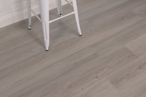 A white metal stool with black-tipped legs on a floor with light gray wood grain planks, next to a white baseboard.