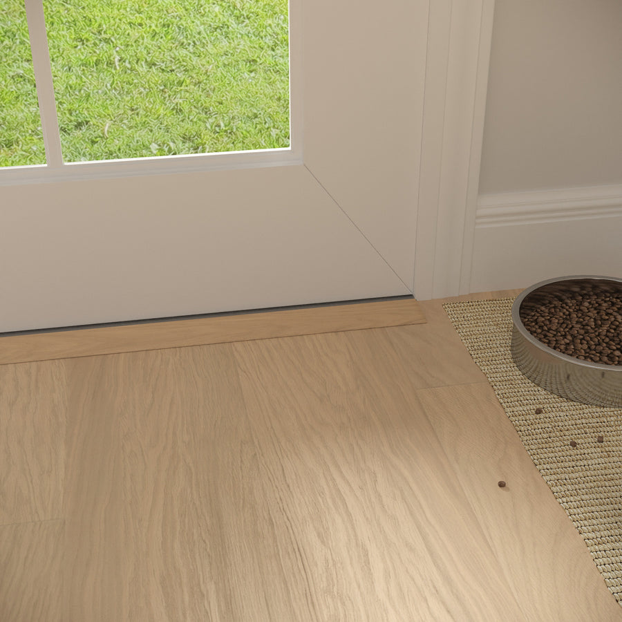 A bowl of dry pet food sits on a woven mat near a glass door, with light wood flooring and green grass visible outside.