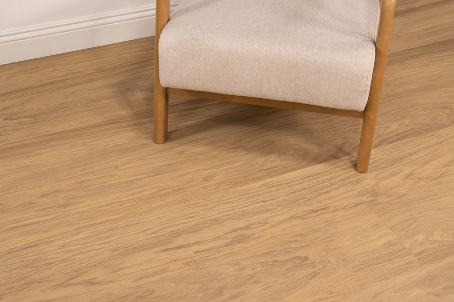 A light wood floor with visible grain patterns, next to a beige upholstered chair with wooden legs and frame, against a white baseboard and wall.