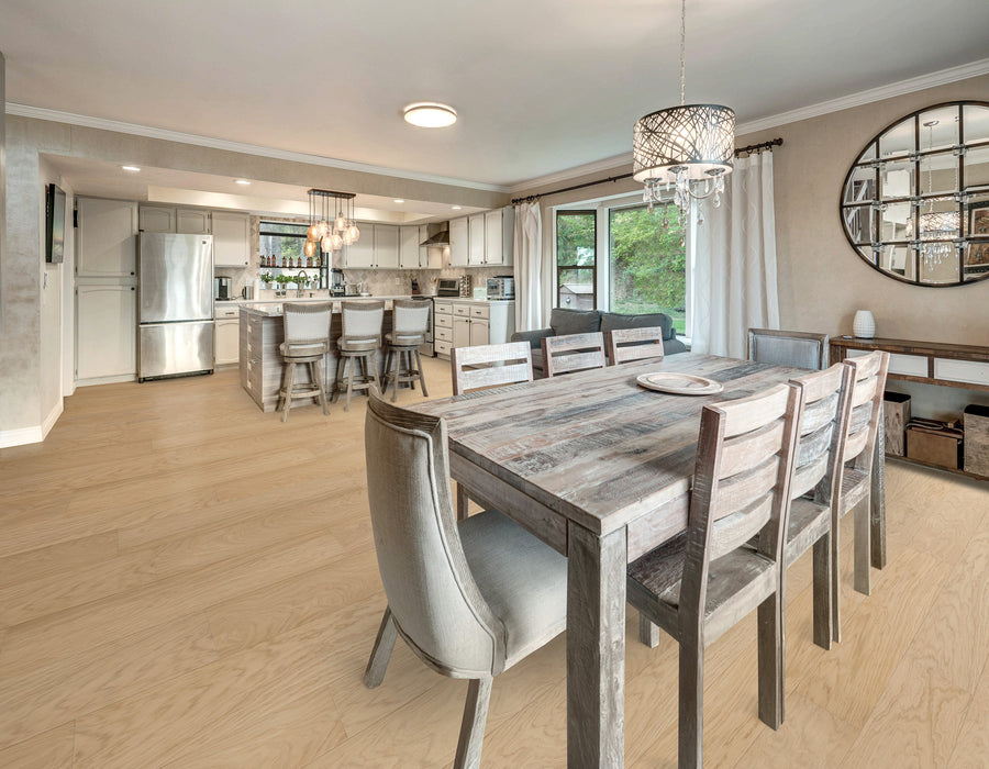 Open-concept kitchen and dining area with a rustic wooden dining table, eight chairs, a modern chandelier, large wall mirror, and stainless steel appliances. Light wood floors and sliding glass doors with views outside.