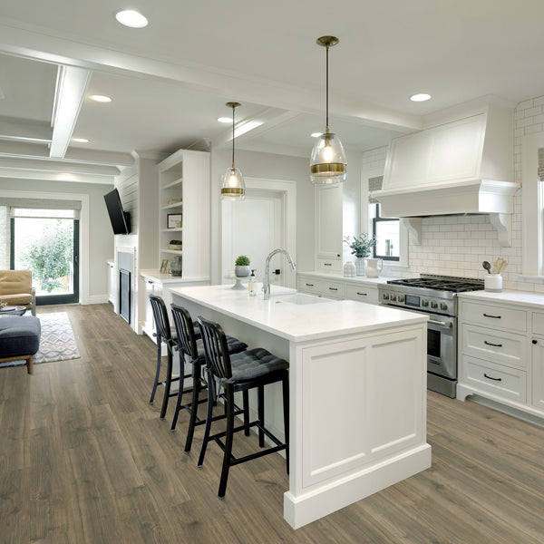 Modern kitchen with white cabinets, a large island with a sink, three black chairs, hanging pendant lights, a gas stove, subway tile backsplash, wooden floors, and an open layout leading to a living area with a sofa and TV.