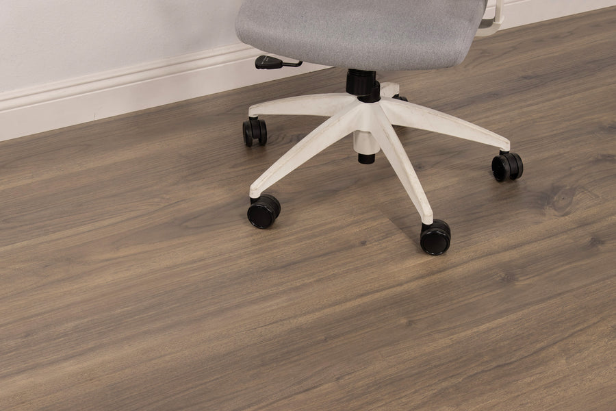 A gray office chair with a white base on black wheels sits on a wood-patterned floor near a white wall and baseboard.