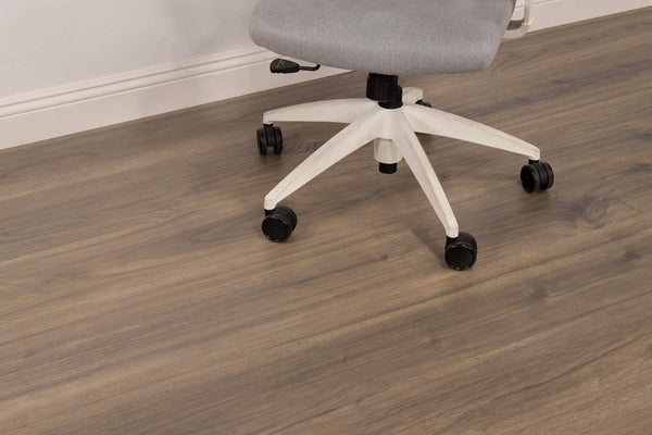 A gray office chair with a white base on black wheels sits on a wood-patterned floor near a white wall and baseboard.