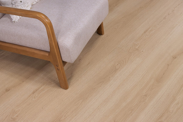 A light wood floor with a beige upholstered chair featuring wooden armrests and legs, positioned in the upper left corner of the image.