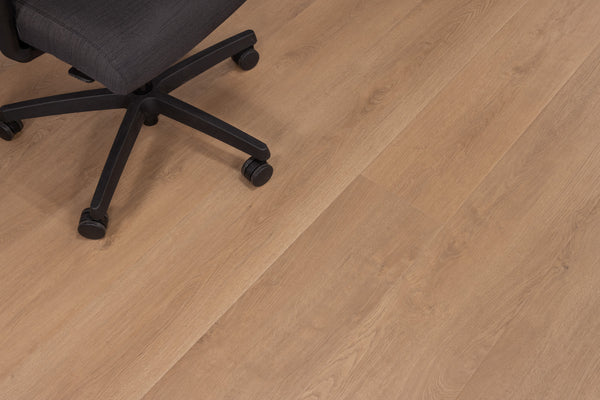 A black office chair with wheels is positioned on a light brown wooden floor. The chair occupies the upper left corner of the image, while the majority of the image shows the wood grain pattern of the floor.