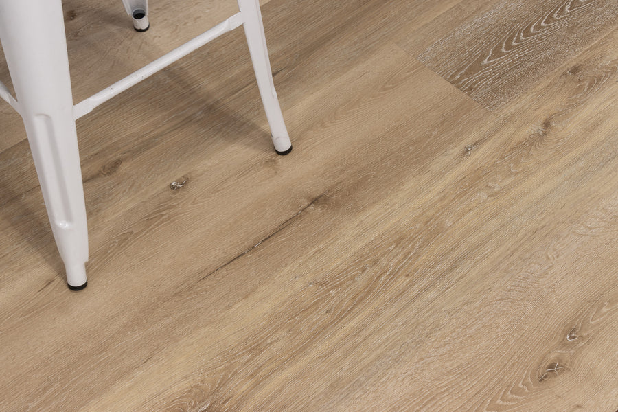 A close-up of light wood grain flooring with part of a white metal chair in the upper left corner.