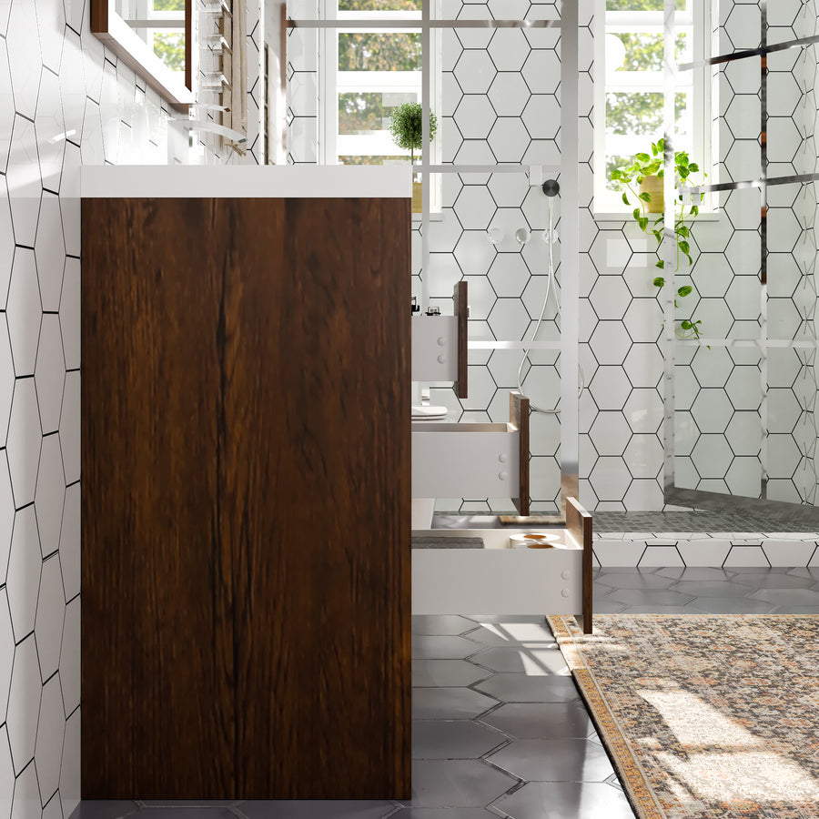 A modern bathroom with white hexagonal tiles, a wooden cabinet, glass shower enclosure, greenery, and a patterned rug on the floor. Sunlight streams in through large windows, creating a bright and airy atmosphere.